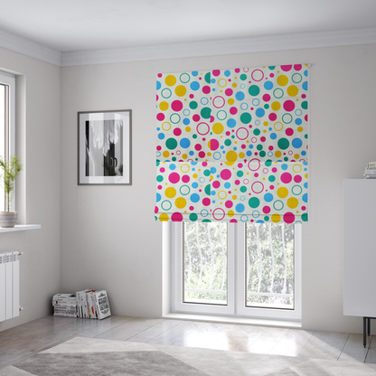 The fabric used to create these Roman blinds is a fun and colourful fabric pattern featuring random solid and hollow polka dots in pink, teal, yellow, and blue on a white background.
