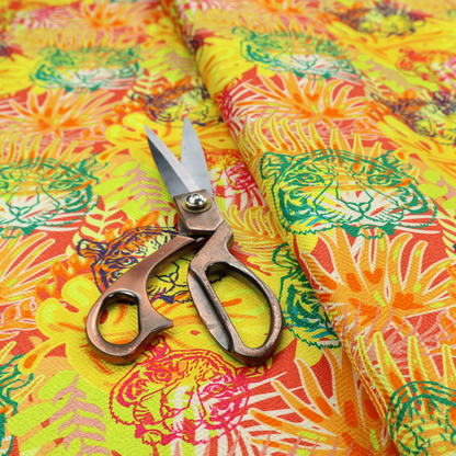 The image features a vibrant, repeating tropical pattern set against a bright yellow and orange background. The design is filled with stylized jungle foliage, including overlapping palm fronds and leaves. Interspersed throughout the pattern are illustrative tiger faces rendered in different colours, including striking shades of green, dark blue, and pinkish-red.   