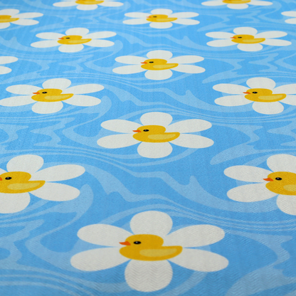 The image features a repeating pattern of white daisies with yellow centres shaped like little rubber ducks, all set against a wavy blue background.   