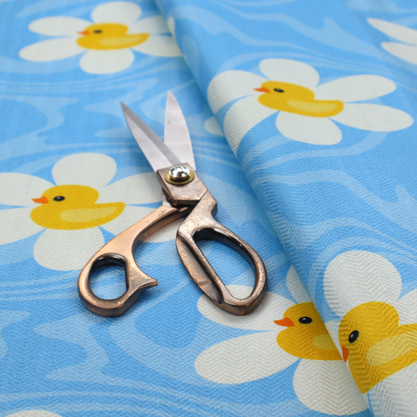 The image features a repeating pattern of white daisies with yellow centres shaped like little rubber ducks, all set against a wavy blue background.   