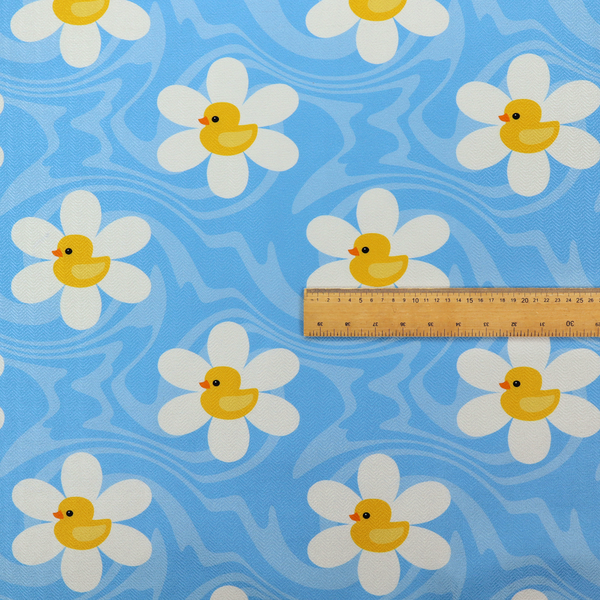 The image features a repeating pattern of white daisies with yellow centres shaped like little rubber ducks, all set against a wavy blue background.   
