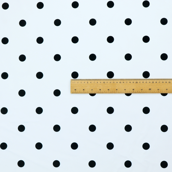 A white fabric pattern featuring evenly spaced black polka dots arranged in horizontal and vertical rows.