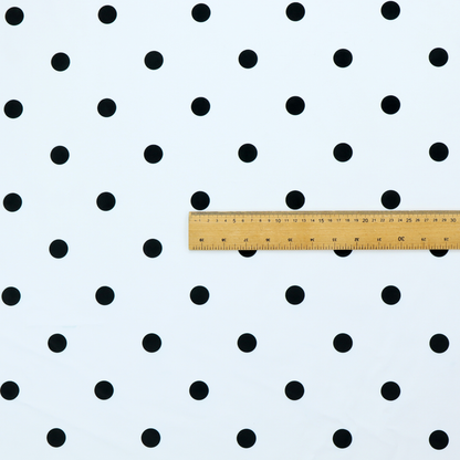 A white fabric pattern featuring evenly spaced black polka dots arranged in horizontal and vertical rows.