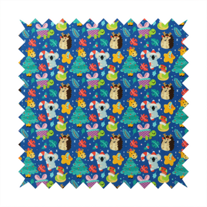 A repeating festive Christmas print on a royal blue background featuring cute cartoon holiday characters, including koalas wearing Santa hats, hedgehogs with antlers, giraffes, Christmas trees, wrapped presents, and stars.   
