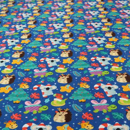 A repeating festive Christmas print on a royal blue background featuring cute cartoon holiday characters, including koalas wearing Santa hats, hedgehogs with antlers, giraffes, Christmas trees, wrapped presents, and stars.   