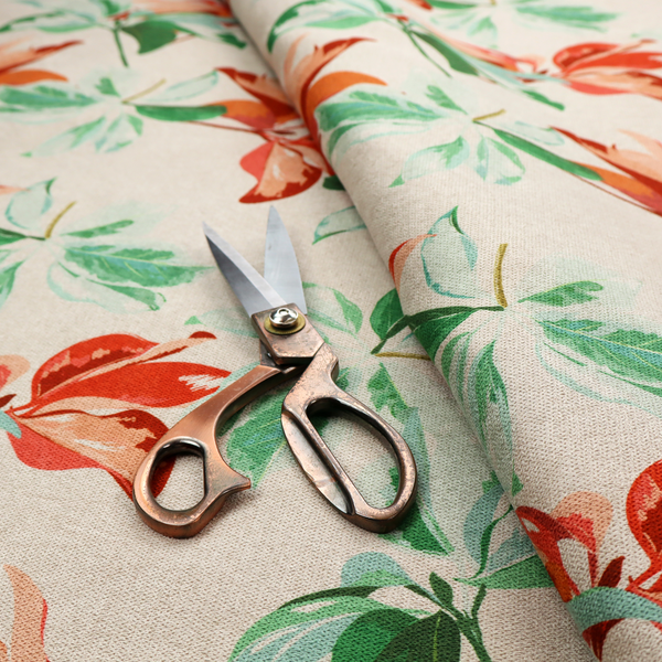 A botanical upholstery fabric on a neutral cream background featuring a repeating painterly pattern of leafy branches in shades of vibrant orange, coral, deep green, and pale mint-green.   